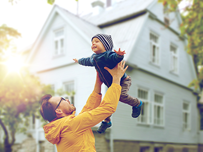 man holding small child aloft in front of house