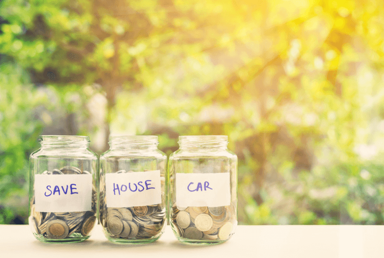 Glass jars labeled "Save" "house" and "car" in an outdoorbackground. 